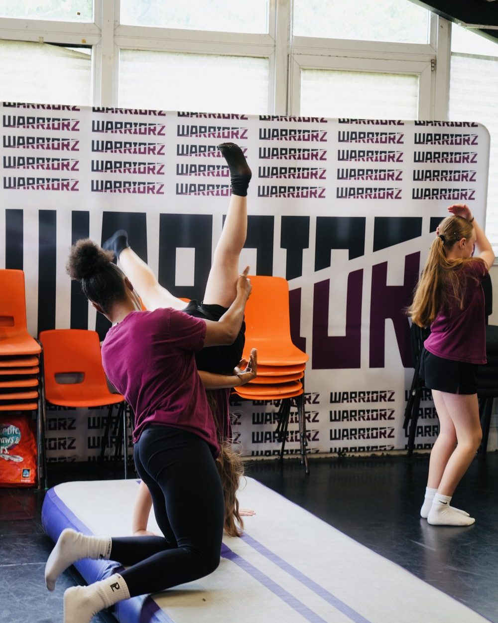 A Warriorz coach spotting a dancer through an inversion on a crash mat